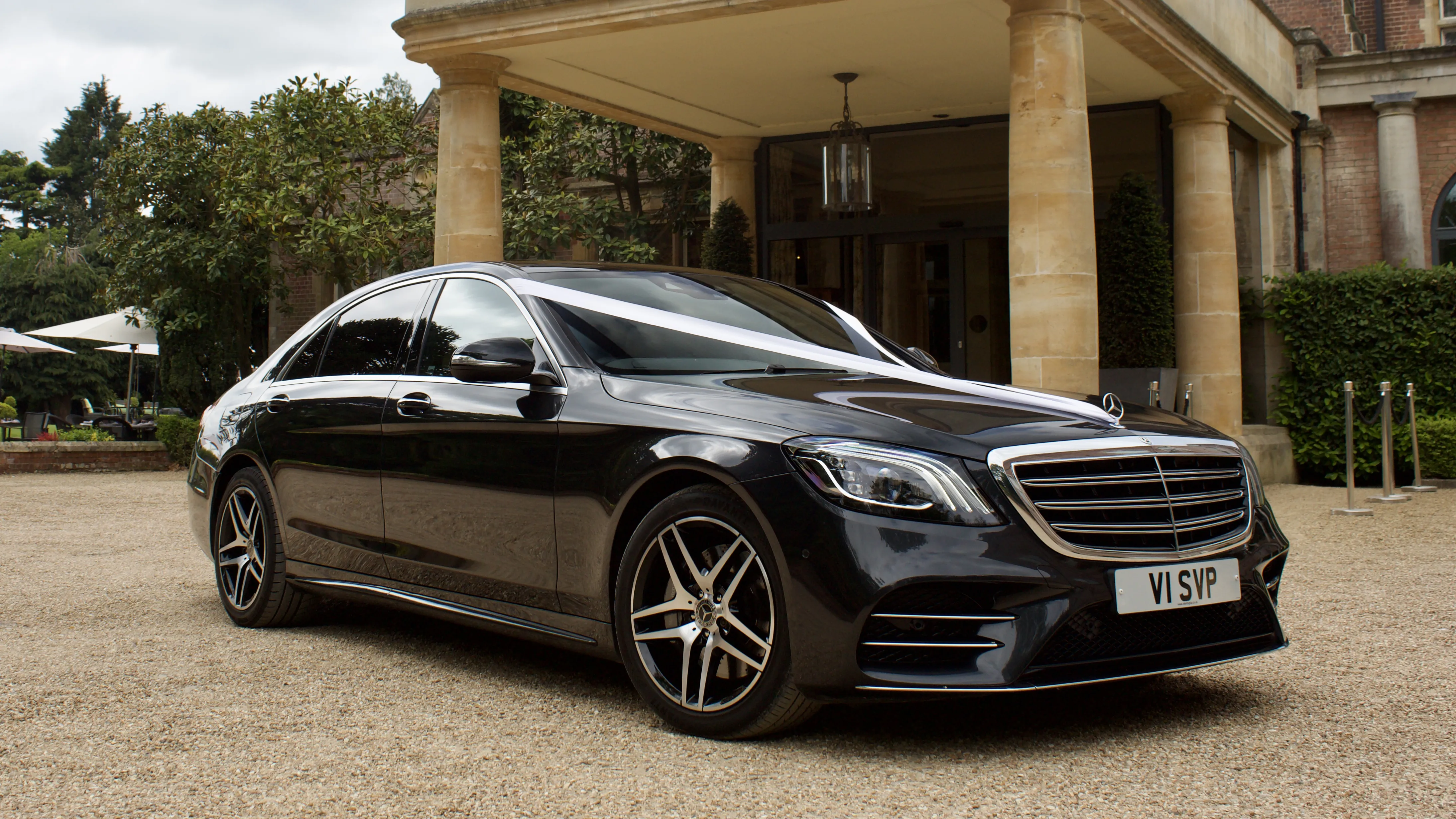 Black Mercedes decorated with White ribbons in front of a wedding venue