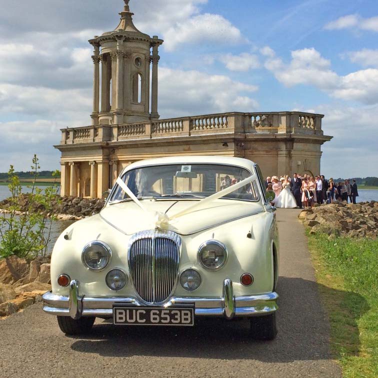 Ivory Daimler 250 V8 decorated with white ribbons. Wedding guests in the background.