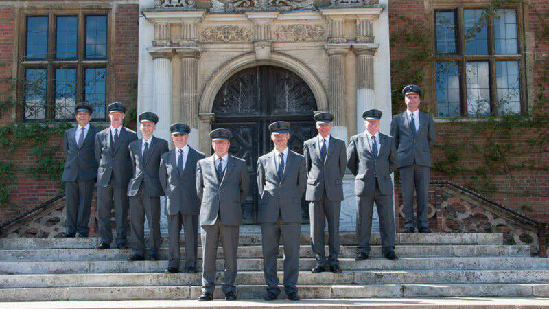 Selection of chauffeurs wearing grey suit and hat in front of a wedding venue posing for photos.