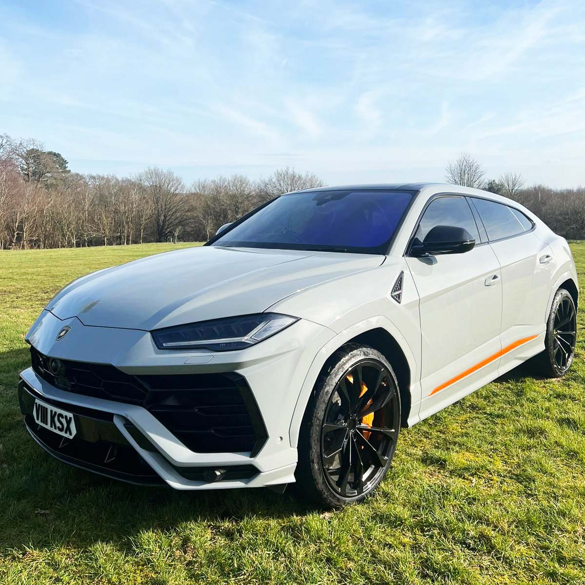 White Lamborghini Urus parked in the middle of a green park with trees in the background
