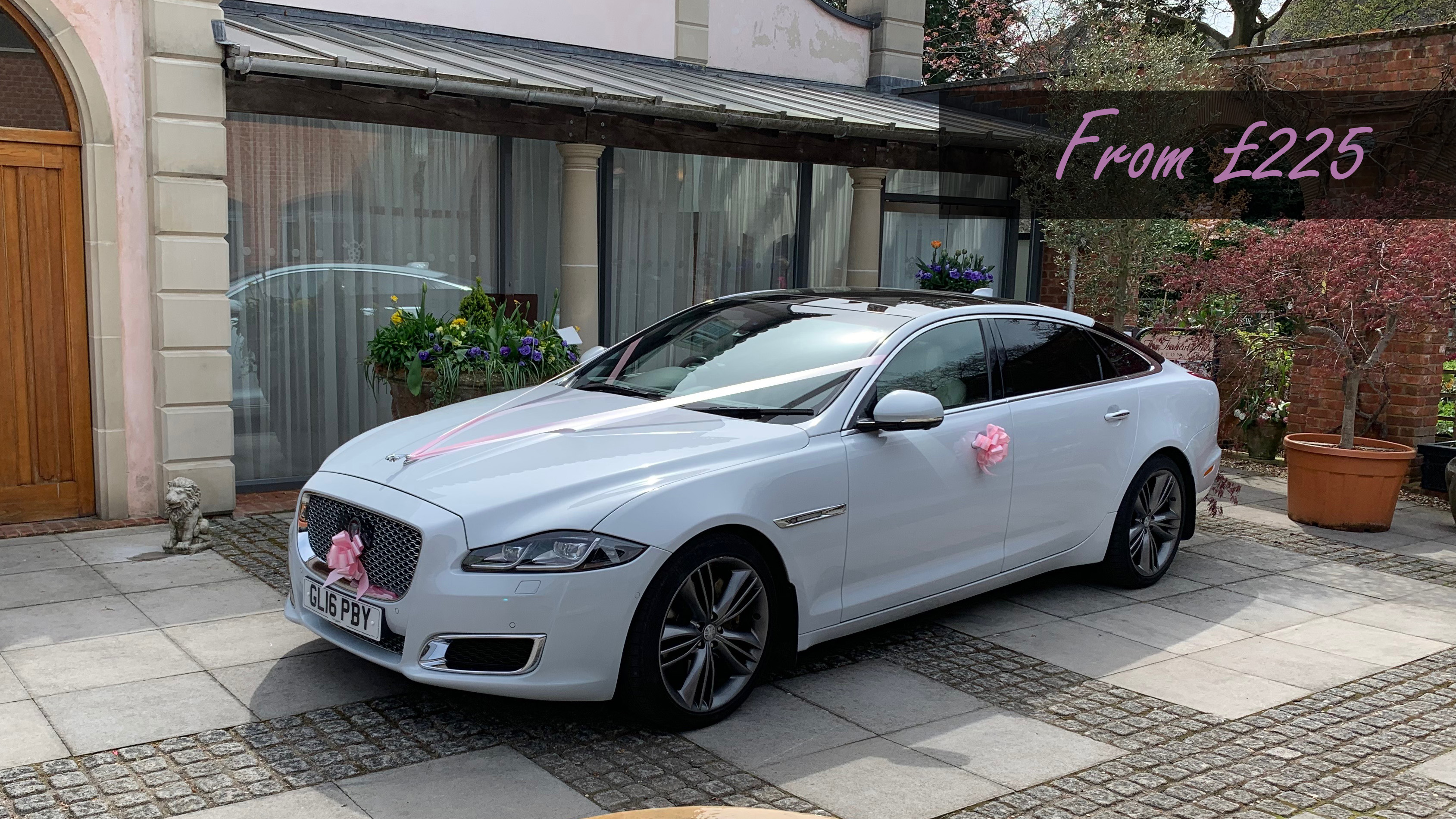 White Jaguar XJ in front of a wedding venue dressed with pale pink ribbons and bows displaying a price from £225.