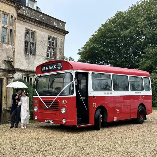 Red Single Decker bus with bride and groom standing in front of the bus.