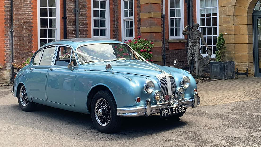 Classic Blue Daimler decorated with white ribbons in front of a wedding venue