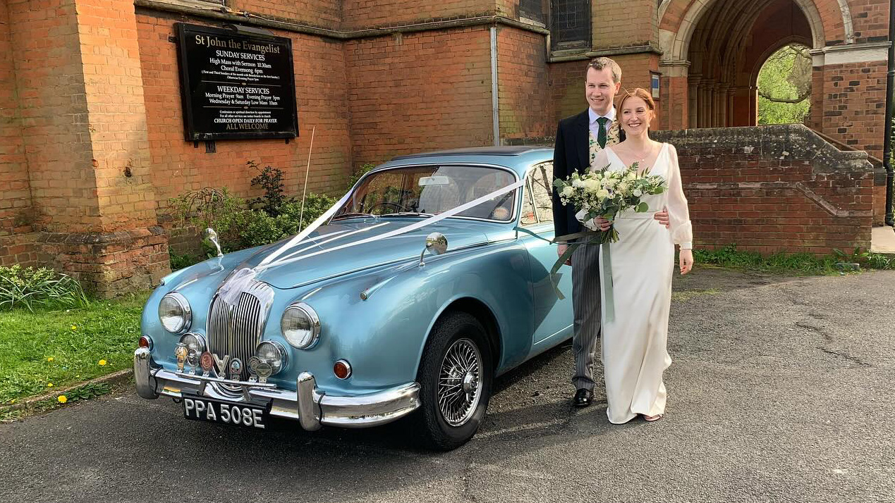 Bride and Groom standing by the Classic Daimler in front of a church