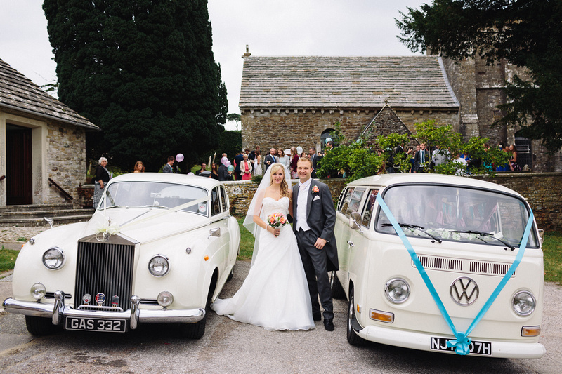 Bride and Groom standing in the middle of two classic vehicles. VW Campervan on the left and Classic Rolls-Royce Silver Cloud on the Right