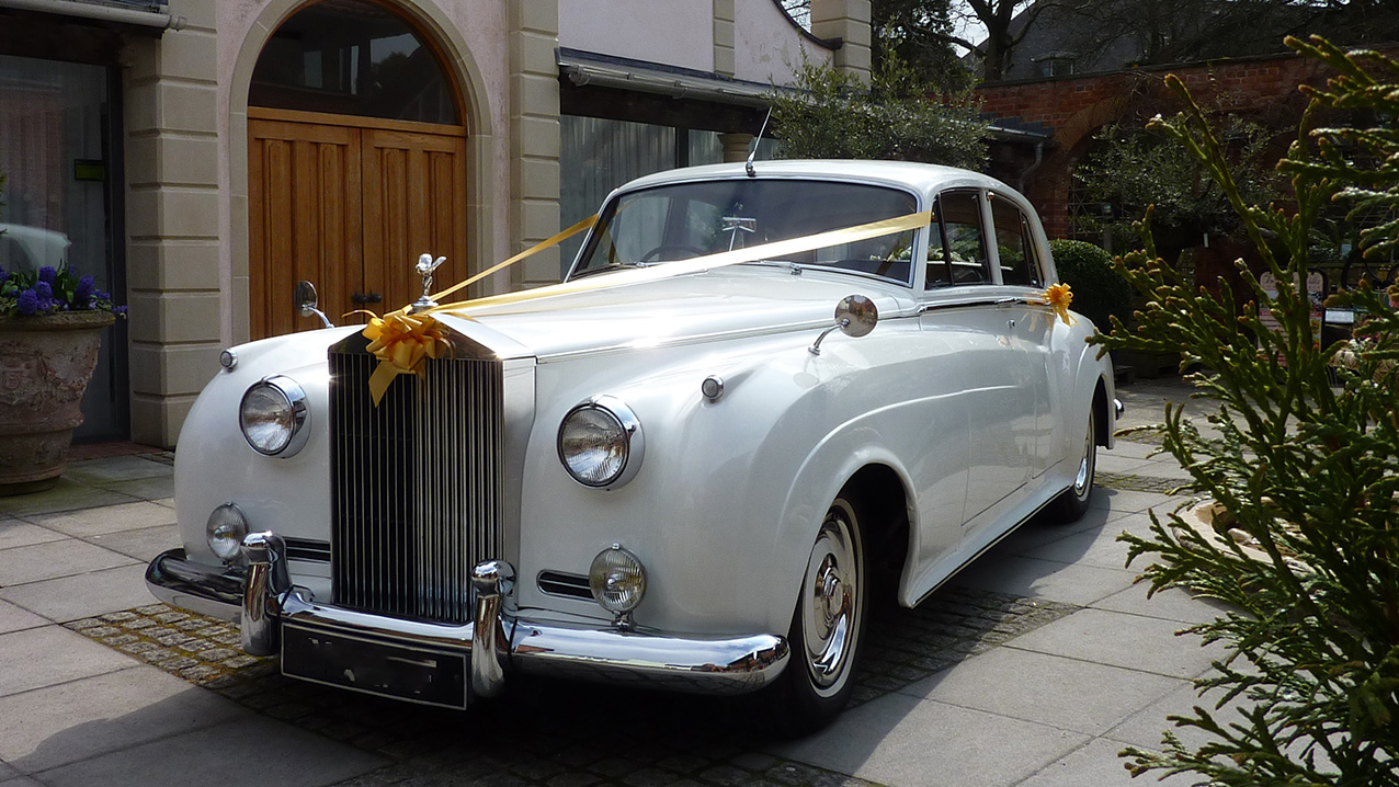 Classic Rolls-Royce Silver Cloud parked outside the Italian Villa in Poole. Vehicle is dressed with Gild Ribbons across its bonnet and matching Gold bows on top of its radiator and door handles.