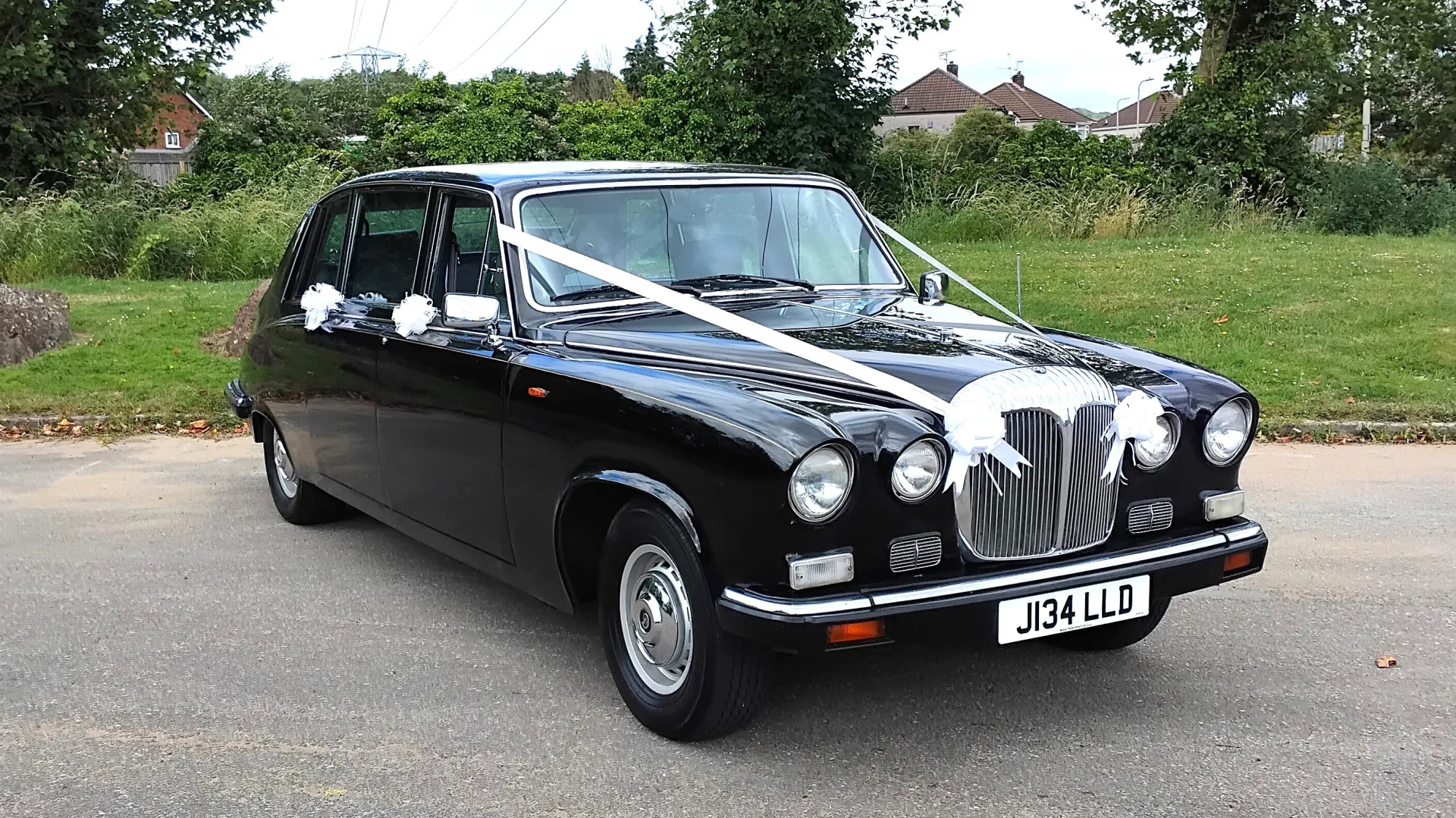 Front view of Black Daimler DS420 Limousinedressed with traditional white ribbons and wite bows on door handles