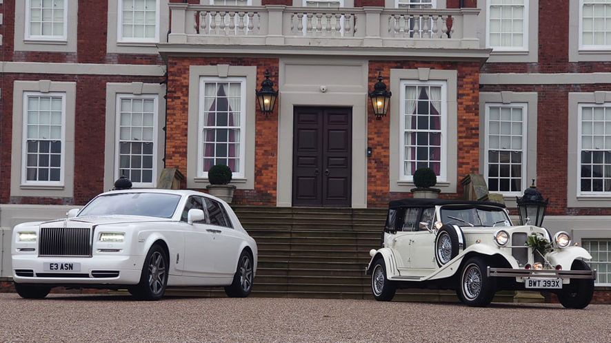 A Modern Rolls-Royce in White on the Left and a Vintage Beauford Wedding Car on the right parked in front of a wedding venue