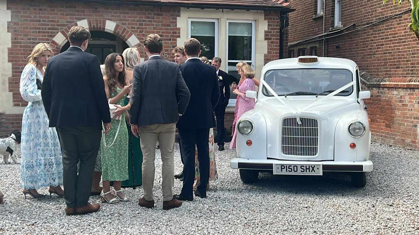 Wedding Guests gathered around a classic taxi cab in white with ribbons