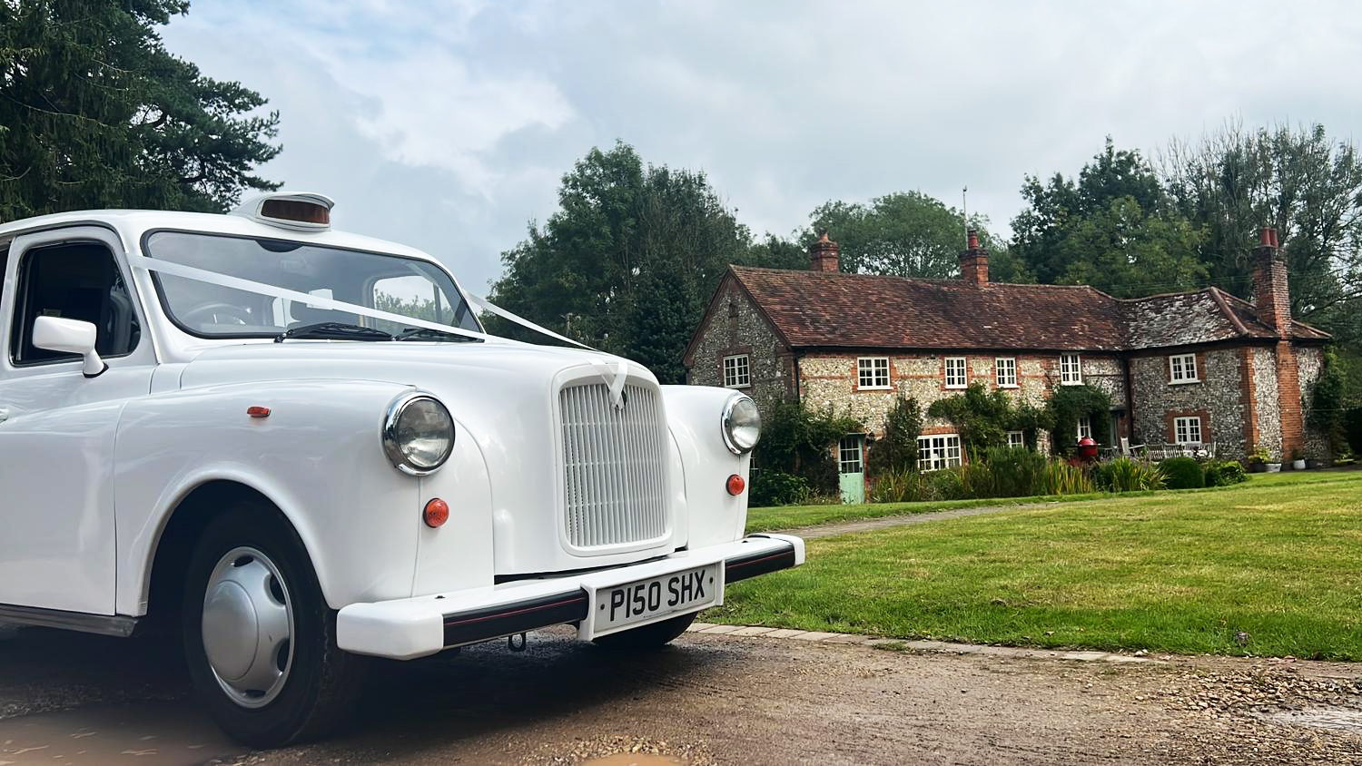 Front view of classic taxi cab decorated with white ribbons in front of a rustic wedding barn.