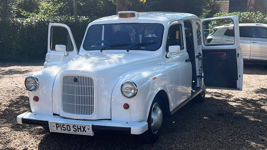 Front view of white classic taxi cab with Orange taxi sign at the top and rear-hinged doors open.