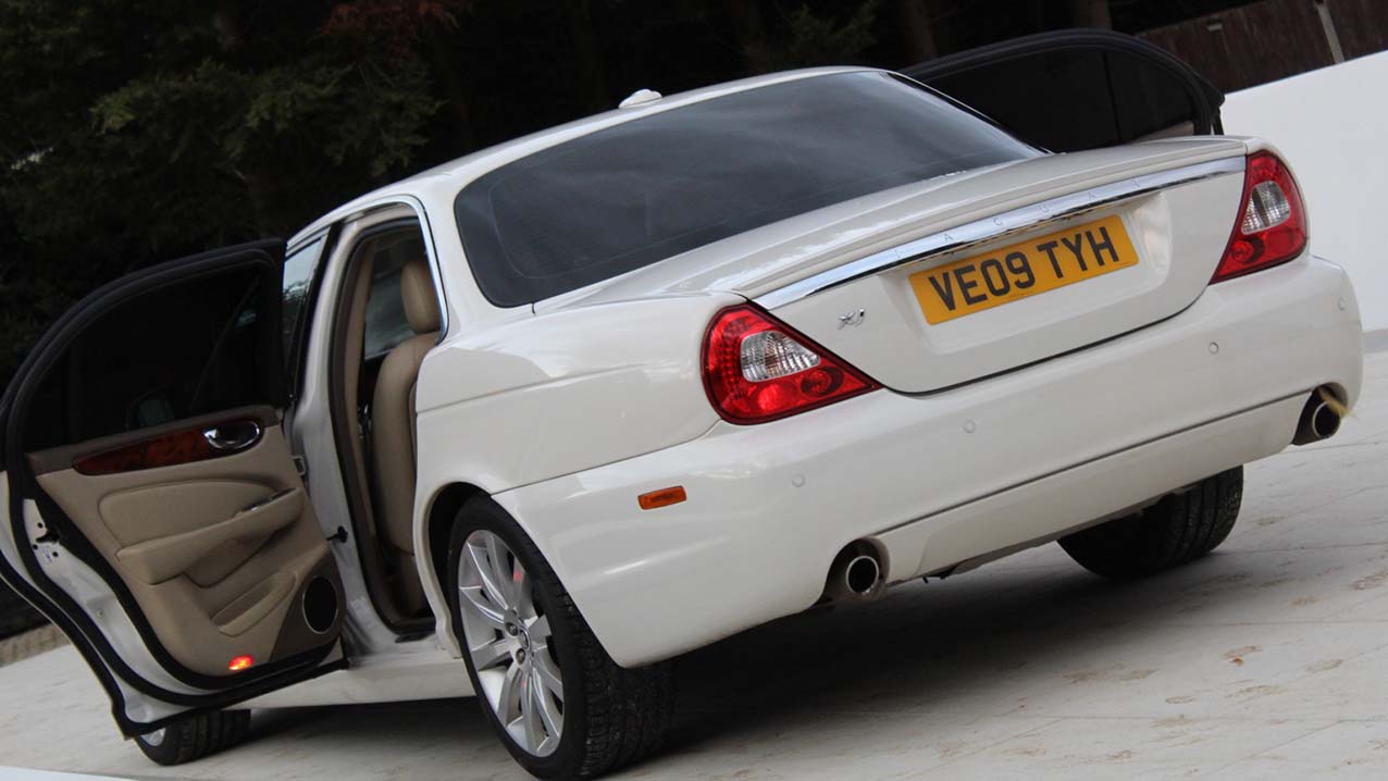 Rear view of White Jaguar XJ with rear left passenger door open showing cream leather interior on door card.