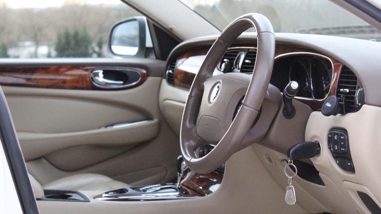 Front interior view of white jaguar XJ with cream leather, wooden door panel and dashboard