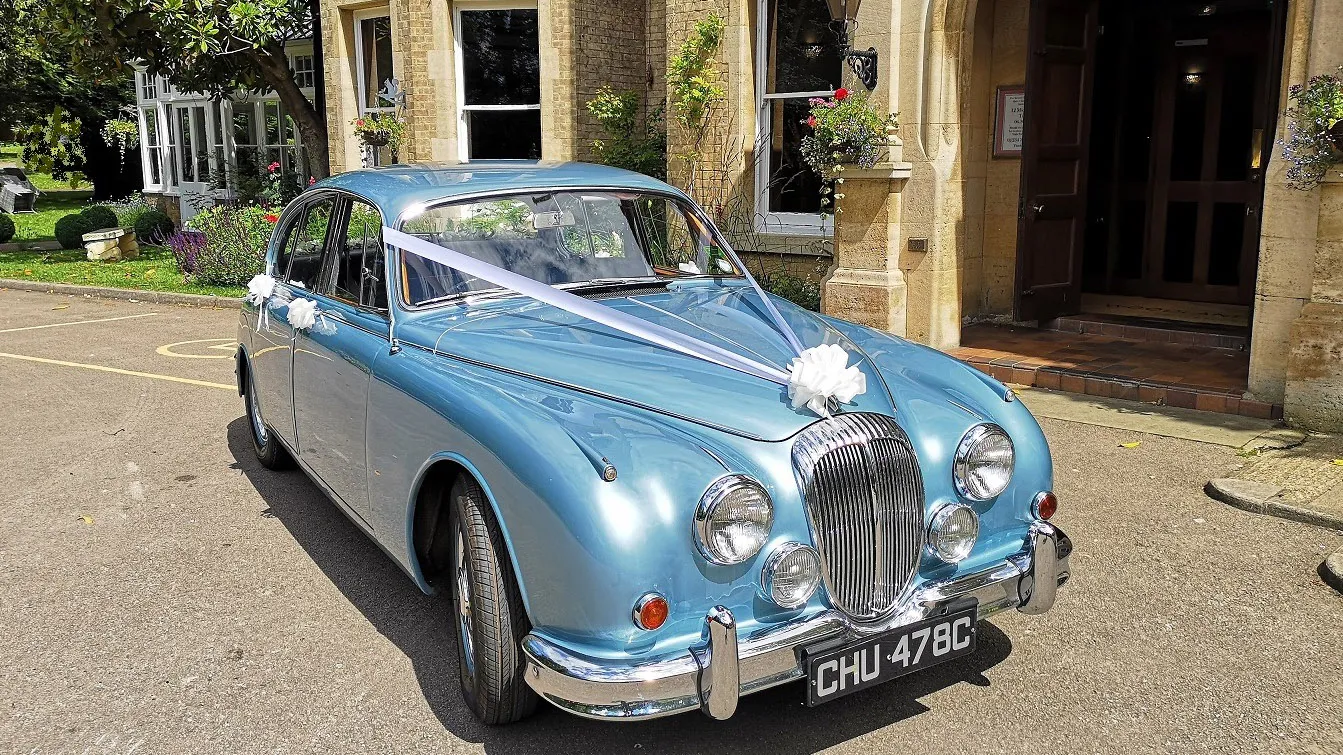 A classic Flitwick-based Jaguar Mk2 in silver blue dressed with traditional V-Shape ribbons in white. White bows on the door handles.