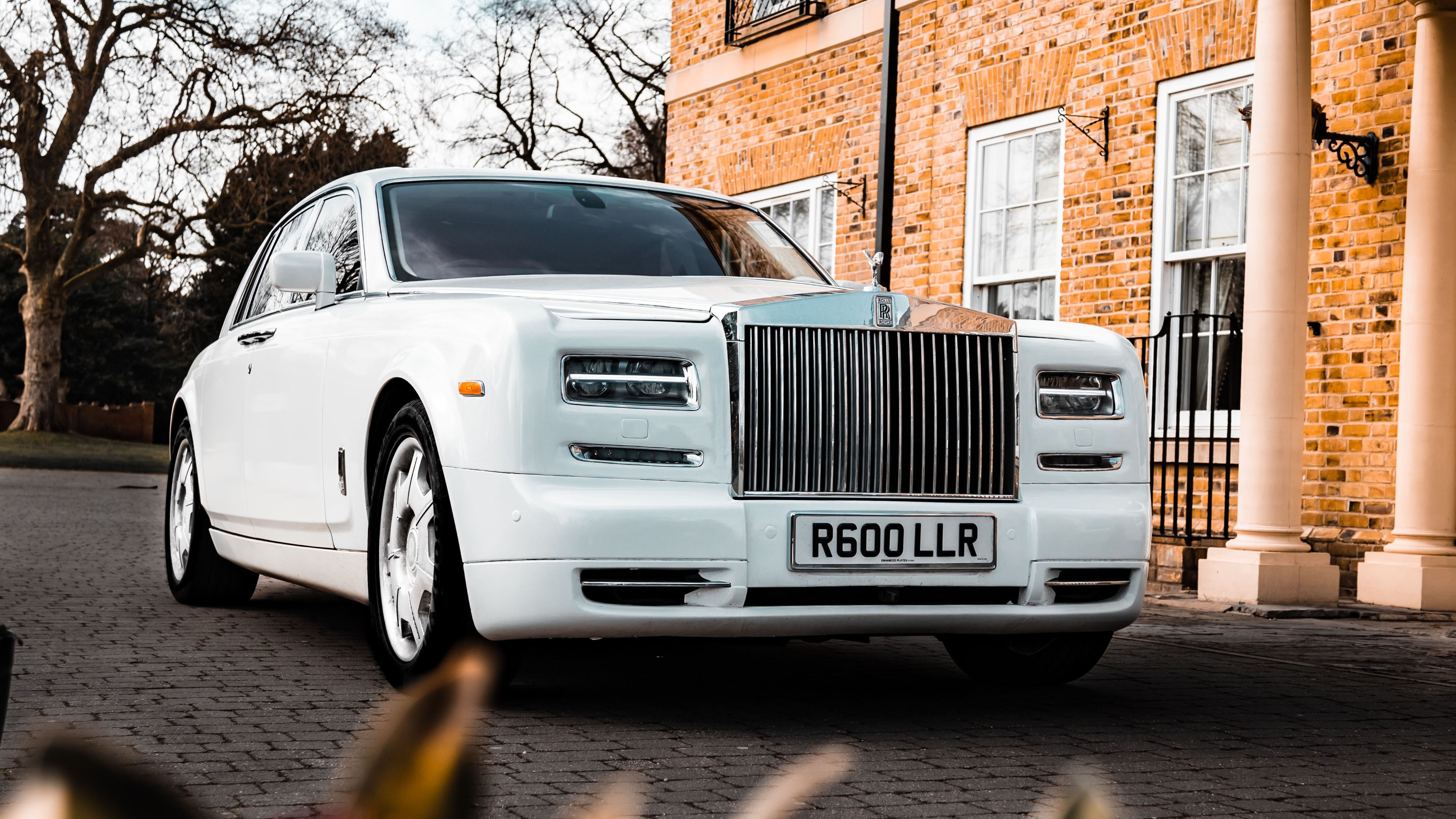 White Rolls-Royce Phantom in front of wedding venue. Front view showing a large Chrome grill and spirit of ecstasy mascot on top.