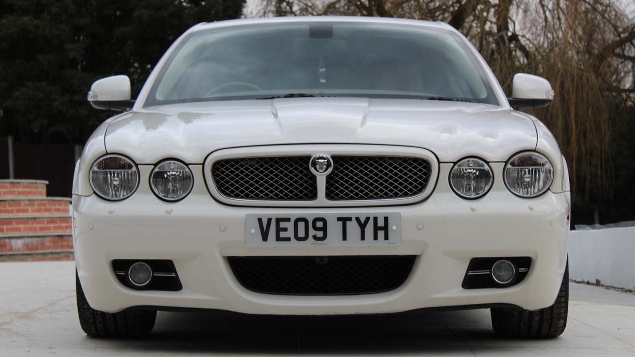 Full front view of white Jaguar XJ with twein headligs and Jaguar badge in the middle of the grill