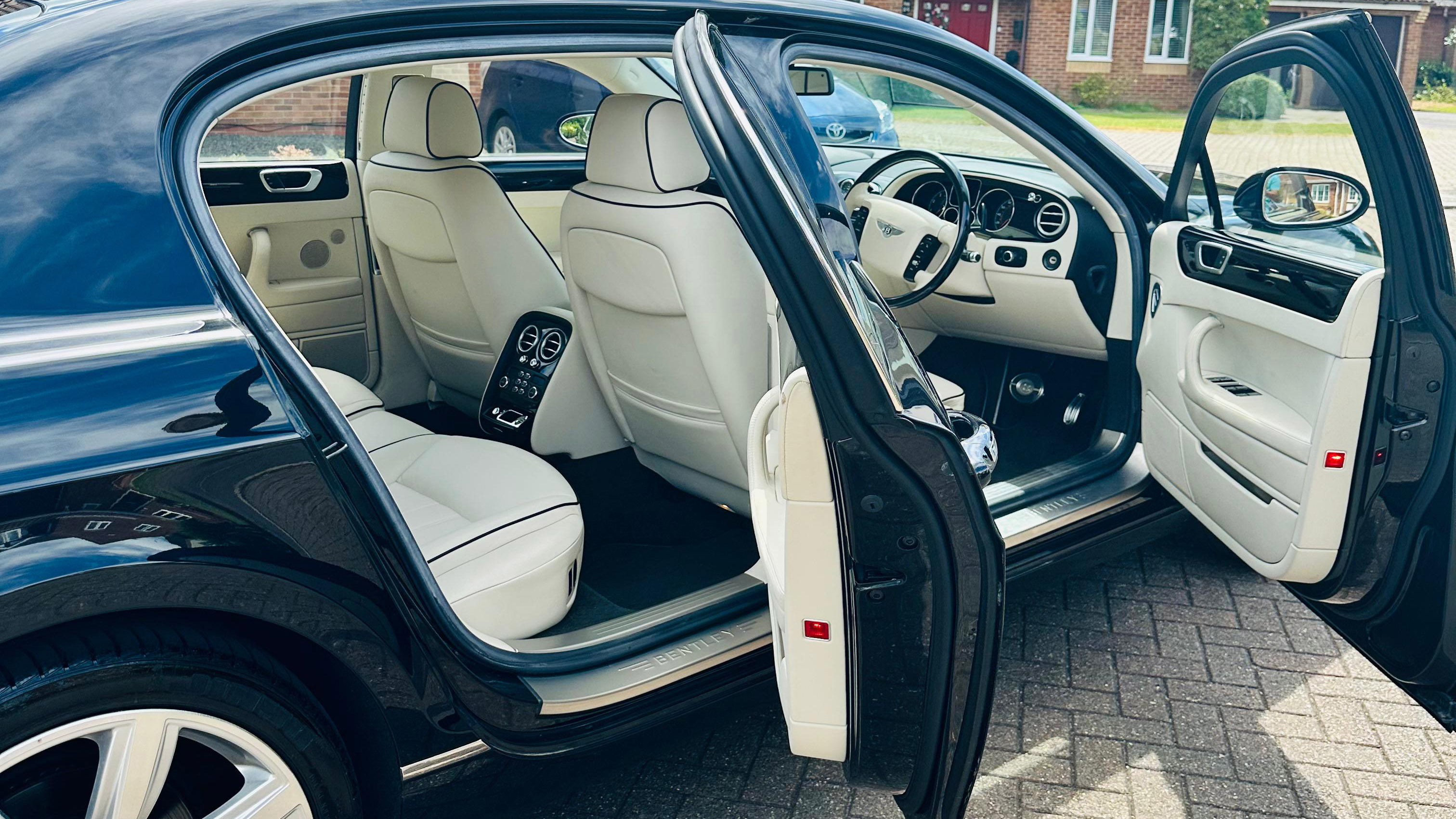 Side view of Black Bentley with both Passenger and driver's doors open showing a cream leather interior