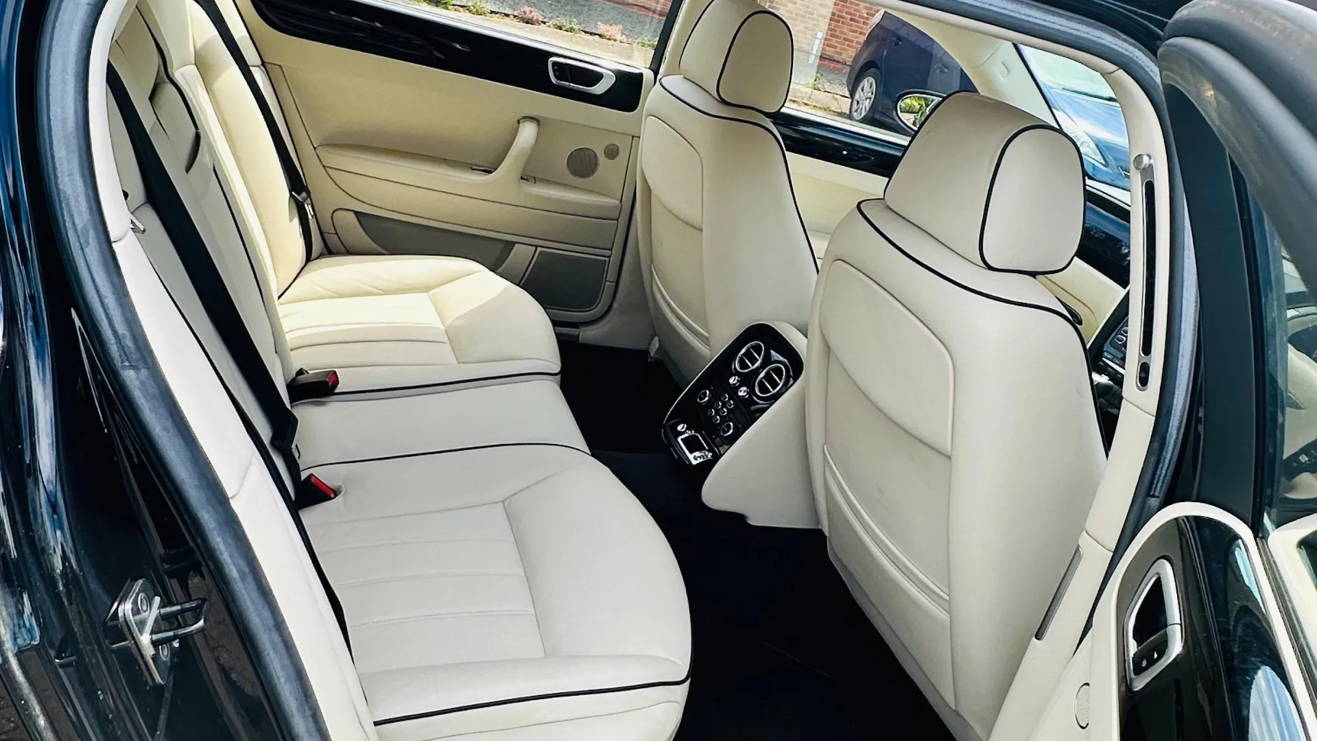 Rear Interior photo inside Bentley Flying Spur showing cream leather interior, large passener legroom and black carpet.