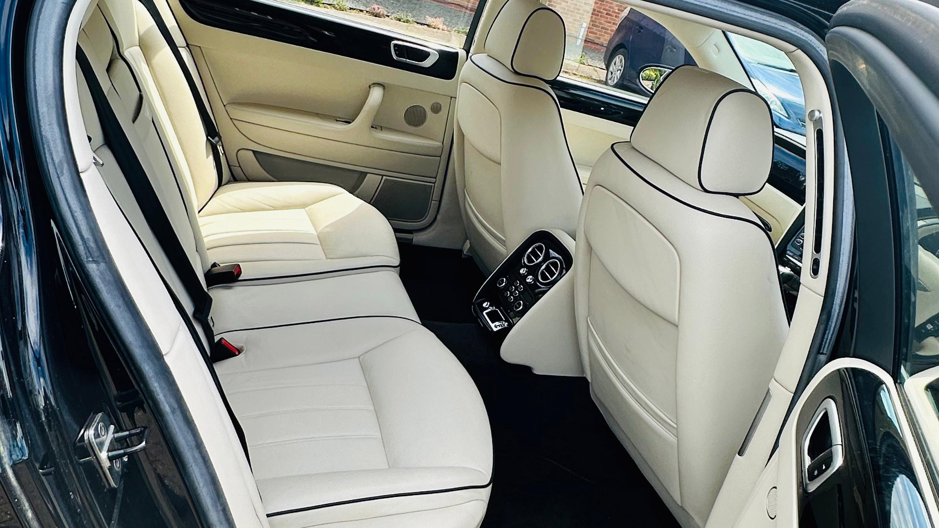 Rear Interior photo inside Bentley Flying Spur showing cream leather interior, large passener legroom and black carpet.