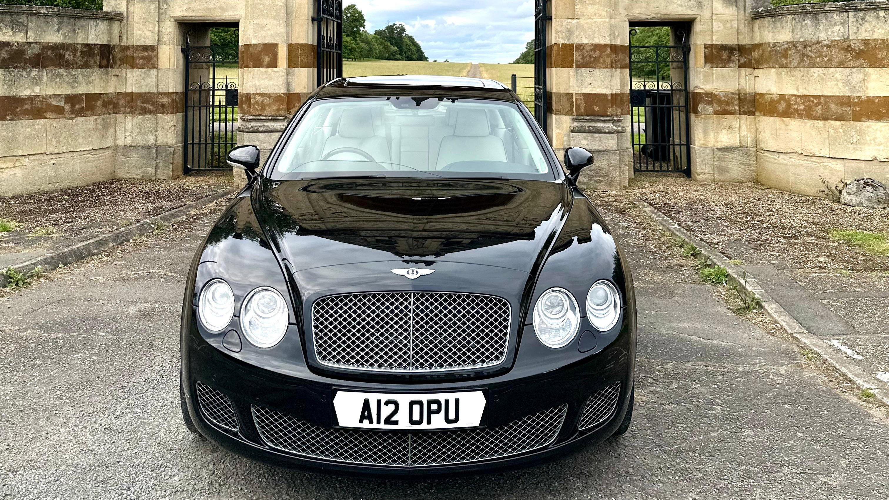 Full front view of Black Bentley Flying Spur with twin headlights, chrome grill and Bentl;ey badge on top