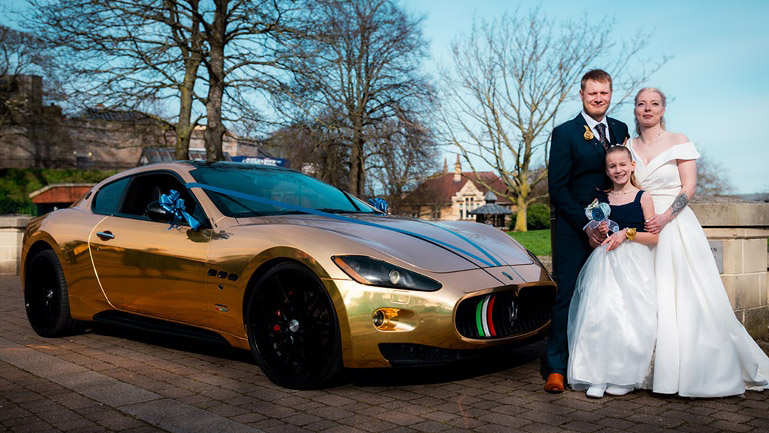 Gold Modern Maserati with Dark Blue Ribbons and Bows with Bride, Groom and their daughter standing in front of the vehicle
