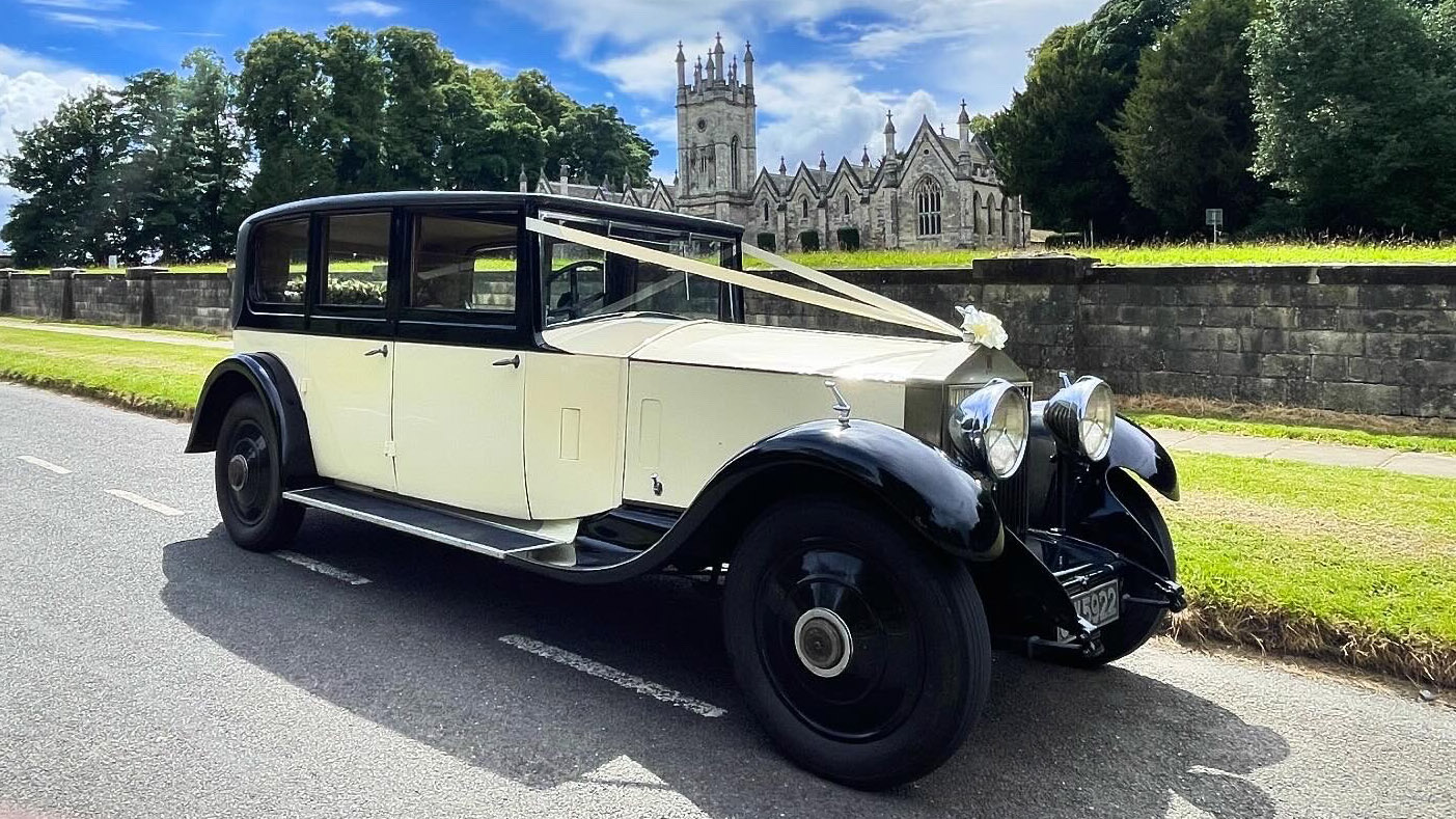 Front side view of Ivory vintage Rolls-Royce with Ivory ribbons on front bonnet, black wheel arches and roof.