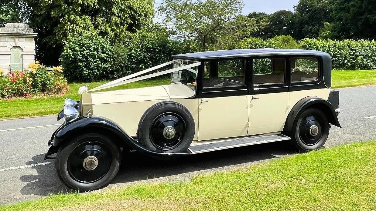 Left view of 1930s vintage Rolls-Royce Phantom in ivory with black wheel arches and roof. Spare wheel mounted on the left side of the vehicle.