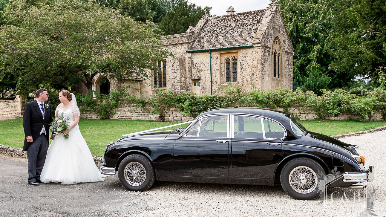 Left Side view of Classic Mk2 Jaguar with Bride and Groom standing in front of the vehicle. Church is in the background.