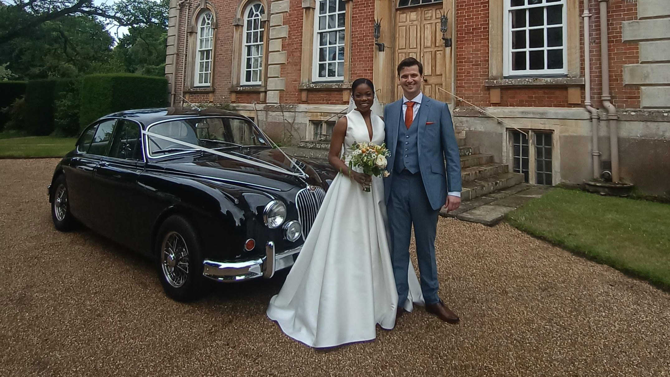 Black Classic Jaguar Mk2 decorated with Ribbons with Bride and Groom standing in front of the vehicle smiling