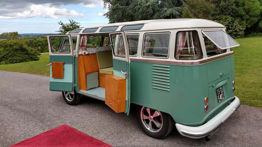 Rear left view of classic campervan with rear doors open and red carpet in front of the door