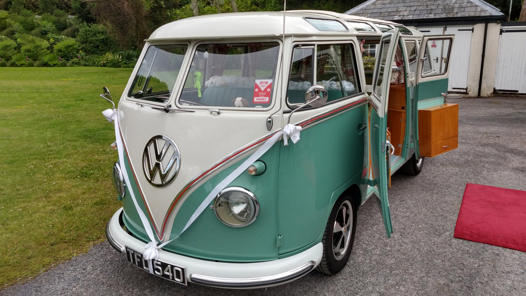 Right front view of vw campervan decorated with white ribbons with rear passenger doors open in front of red carpet