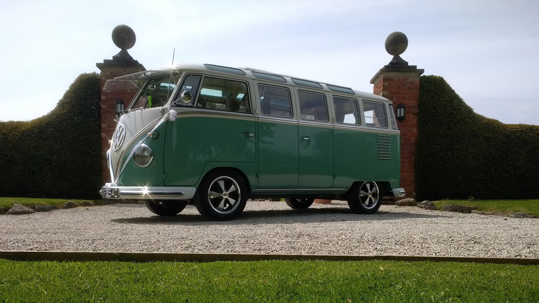 Left side view of Classic campervan in white and pale green in front of a wedding venue main entrance with doors close