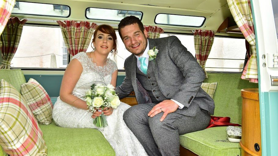 Bride and Groom seating inside the campervan's rear seating area showing a green cloth seats with cushions and  curtains on the windows