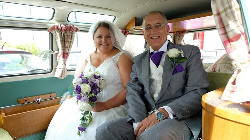 Bride and Father seating inside the campervan. Bride is holding a bouquet of flowers in her hands