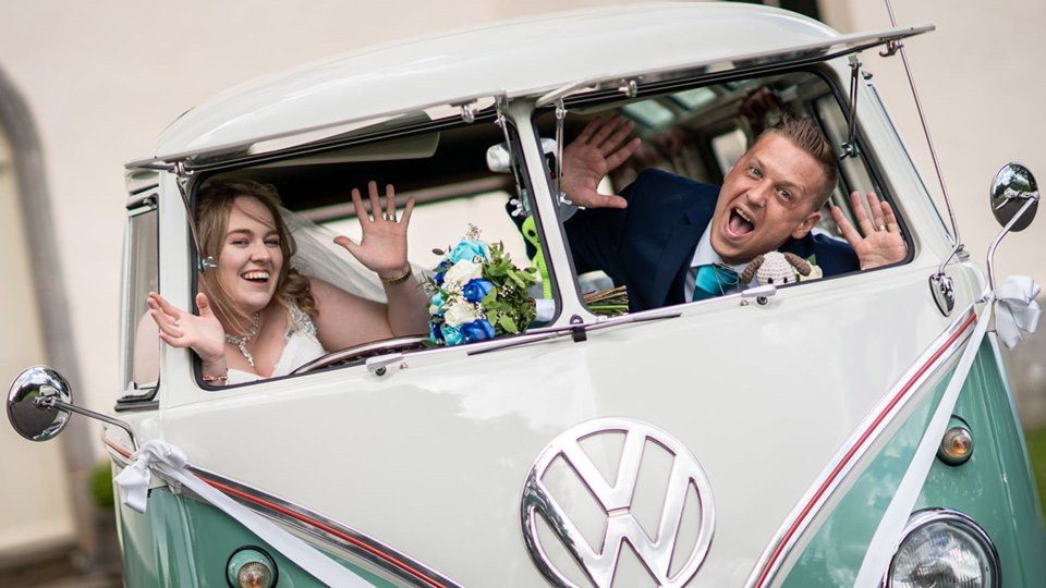 volkswagen campervan with front windows open with bride and groom smiling and making funny faces