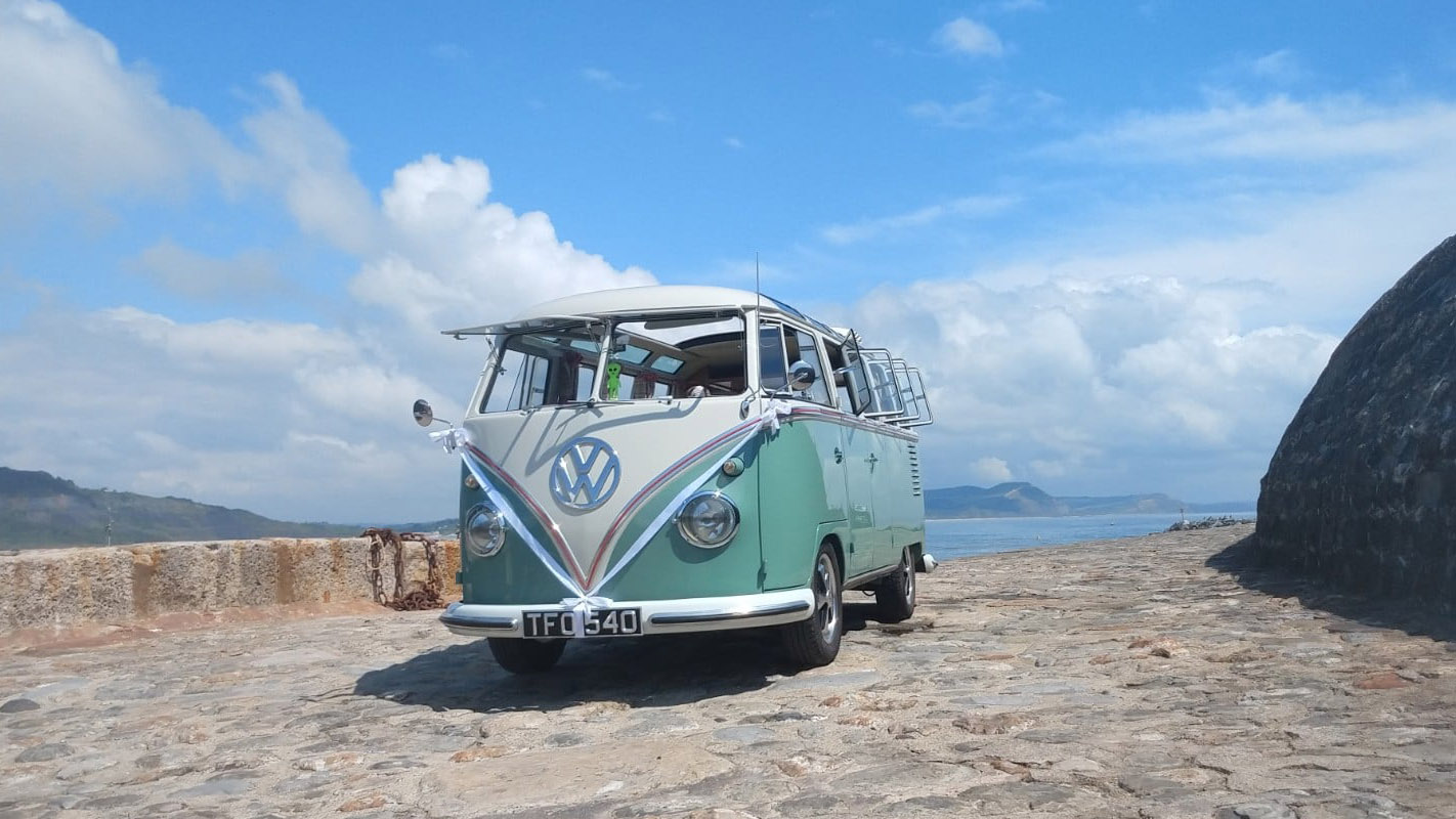 volkswagen campervan decorated with white ribbons with view of Devon Coast in the background