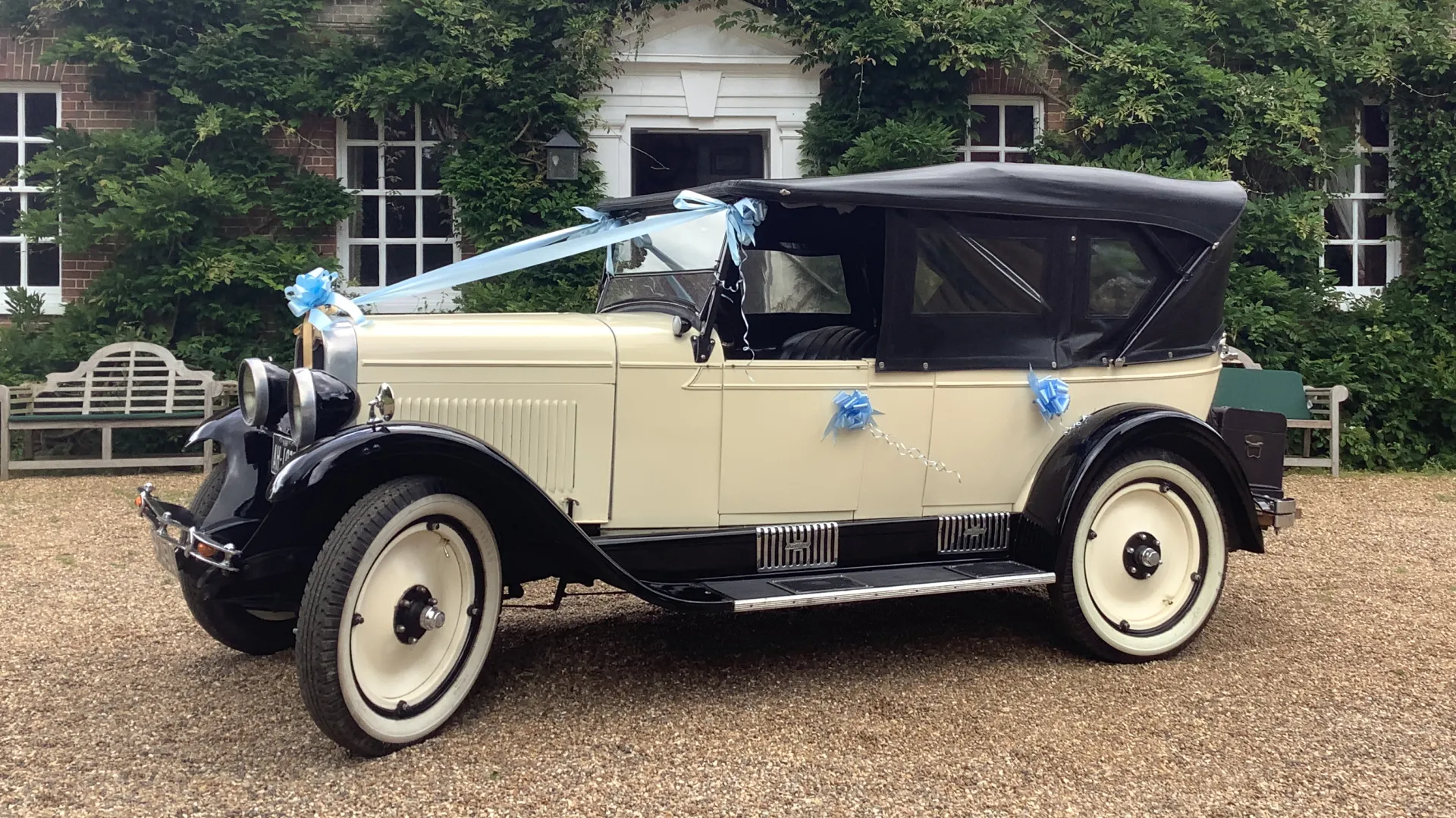 Ivory and Black Chevrolet in front of a wedding venue dressed with light blue ribbons accross the front bonnet and matching bows on door handles