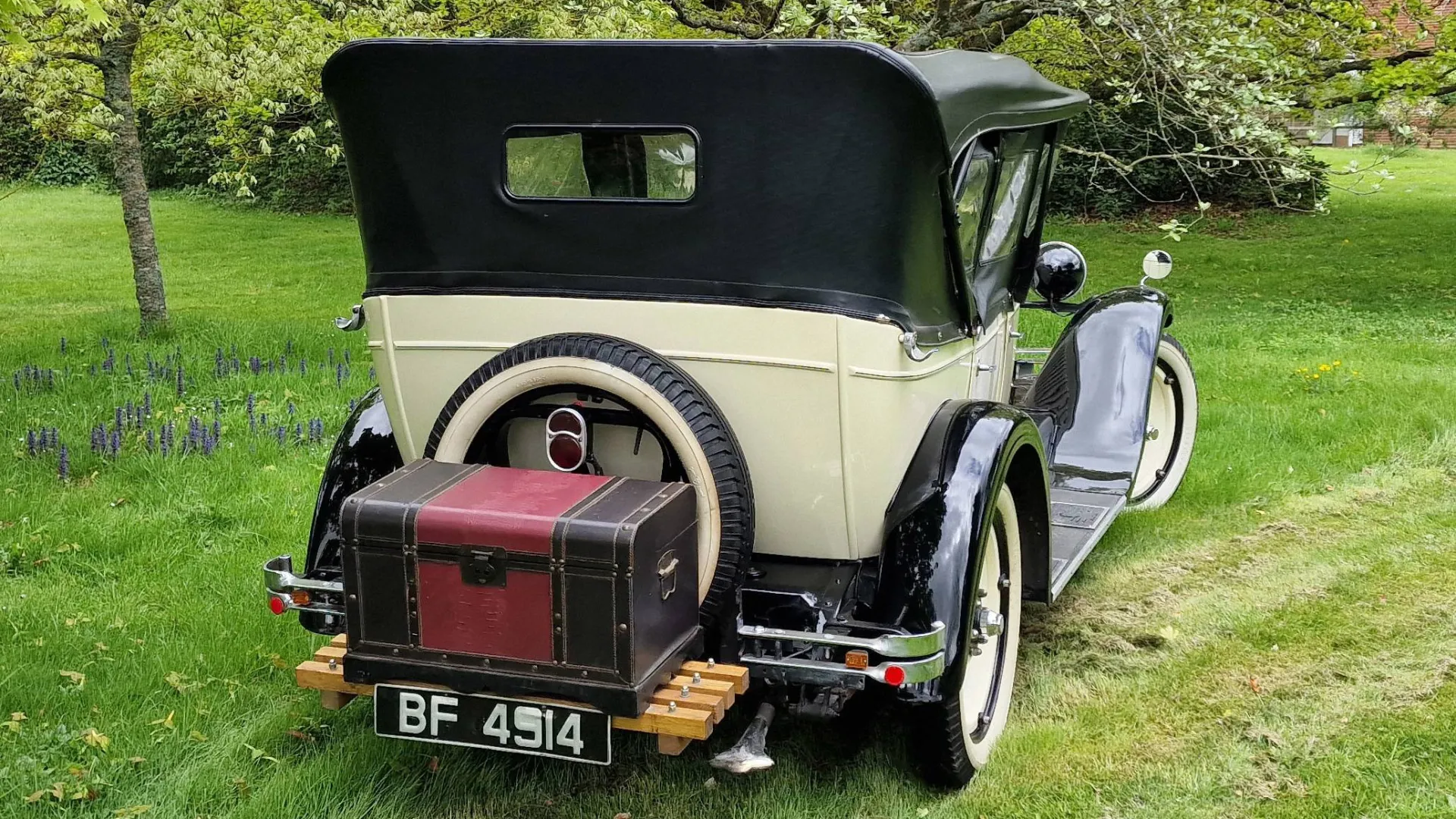 Rear view of Chevrolet with black soft top roof, spare wheel mounted at the rear and a Black and burgungy picnic trunk