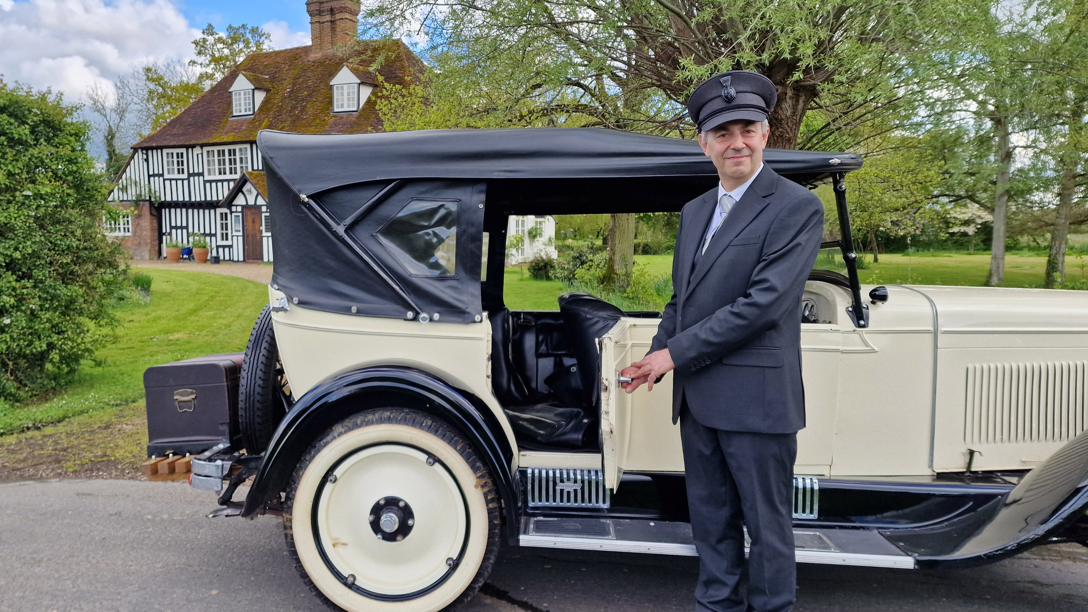 A Smiling fully uniformed chauffeur opening the rear passenger door of the Vintage Chevrolet