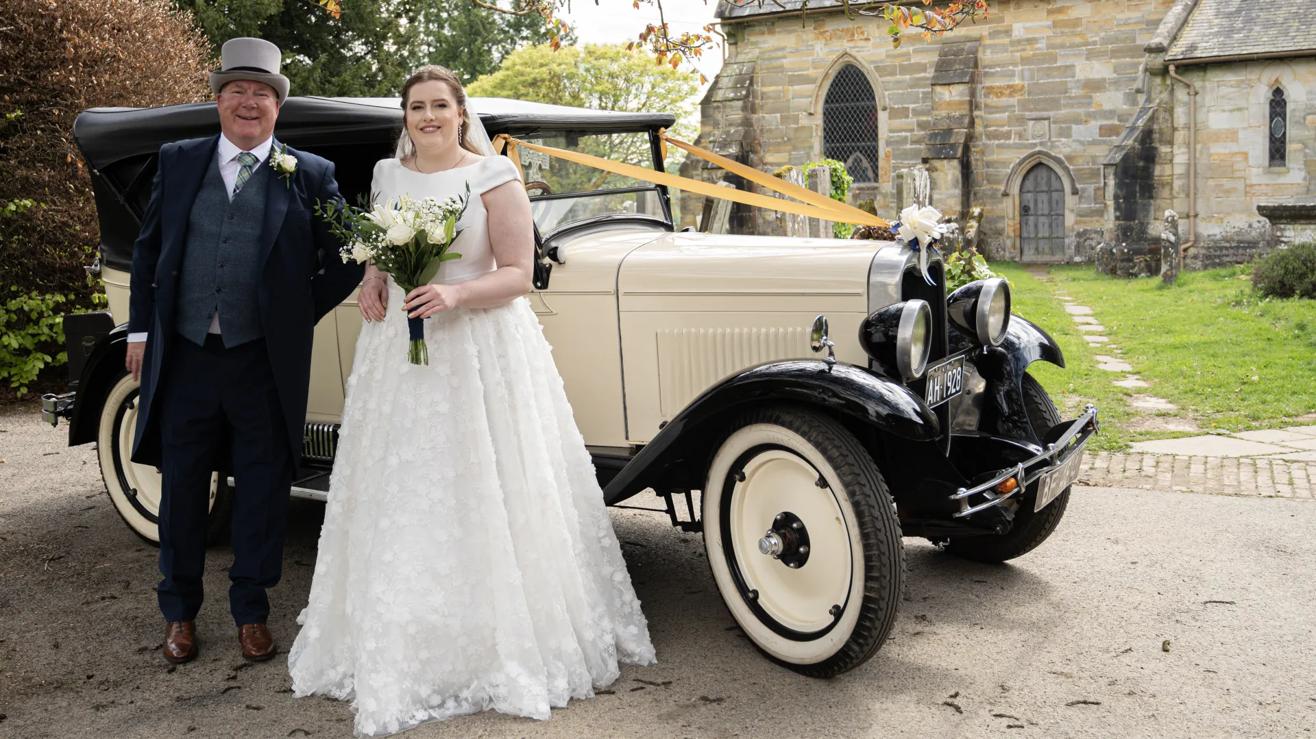 Bride and father standing in front of an ivory vintage car decorated with Gold Ribbons. Car is paked in front of a Church in Tunbridge Wells, Kent.