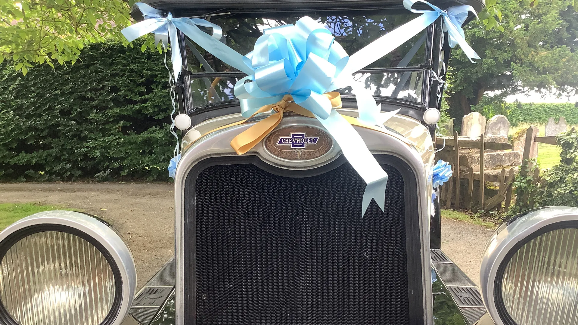 Close up view of the front grill of the vehicle with light blue ribbon and a large bow seating on top of the radiator