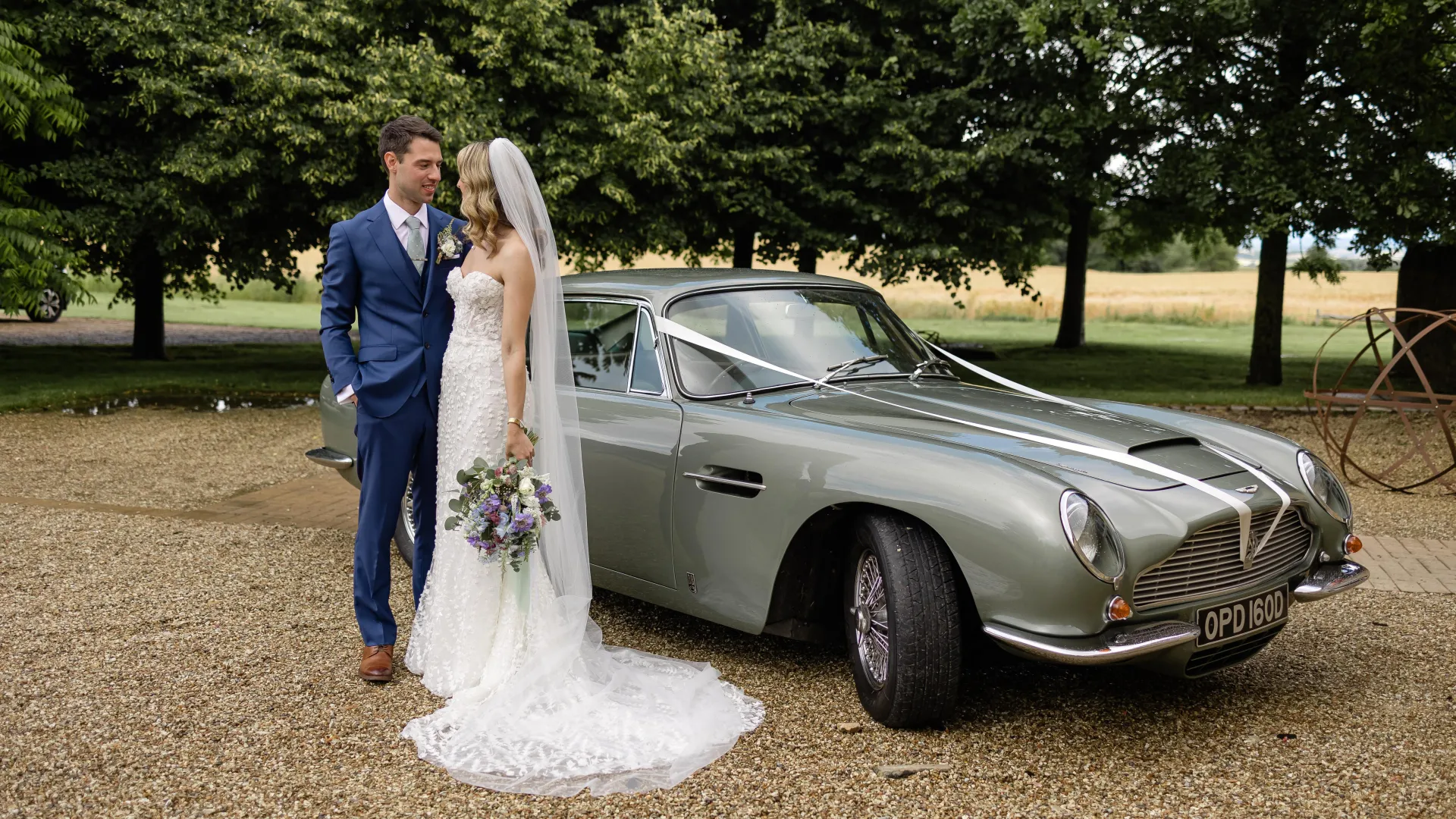 Bride and Groom standing in front of a classic Aston Martin DB6 in Pale Metallic Green