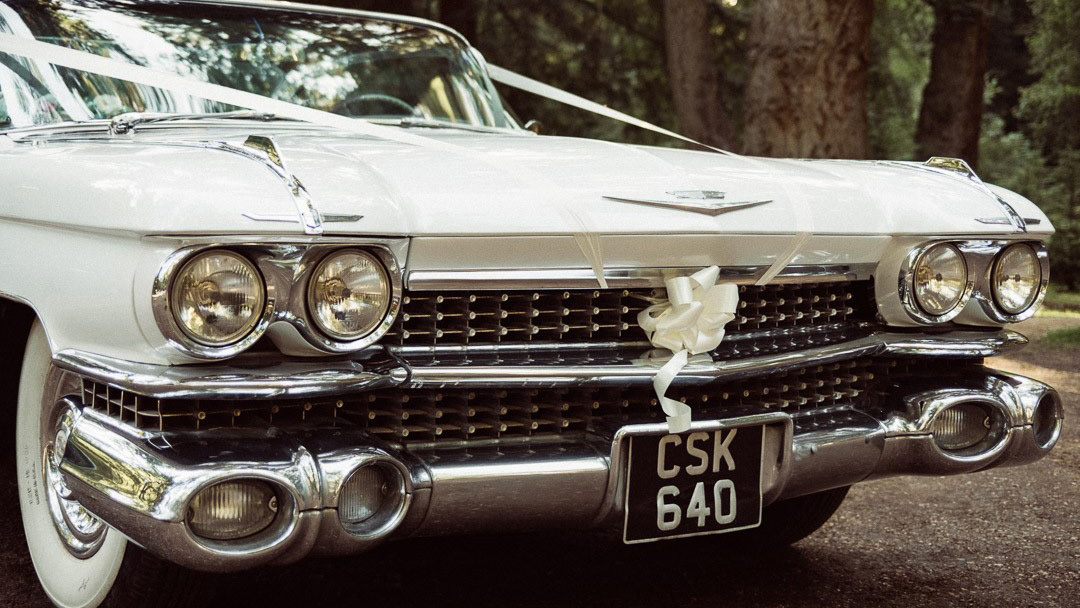 Front grill view of Cadillac with chrome grill and bumper. Decorated with White ribbons and a bow in the middle of the grill.