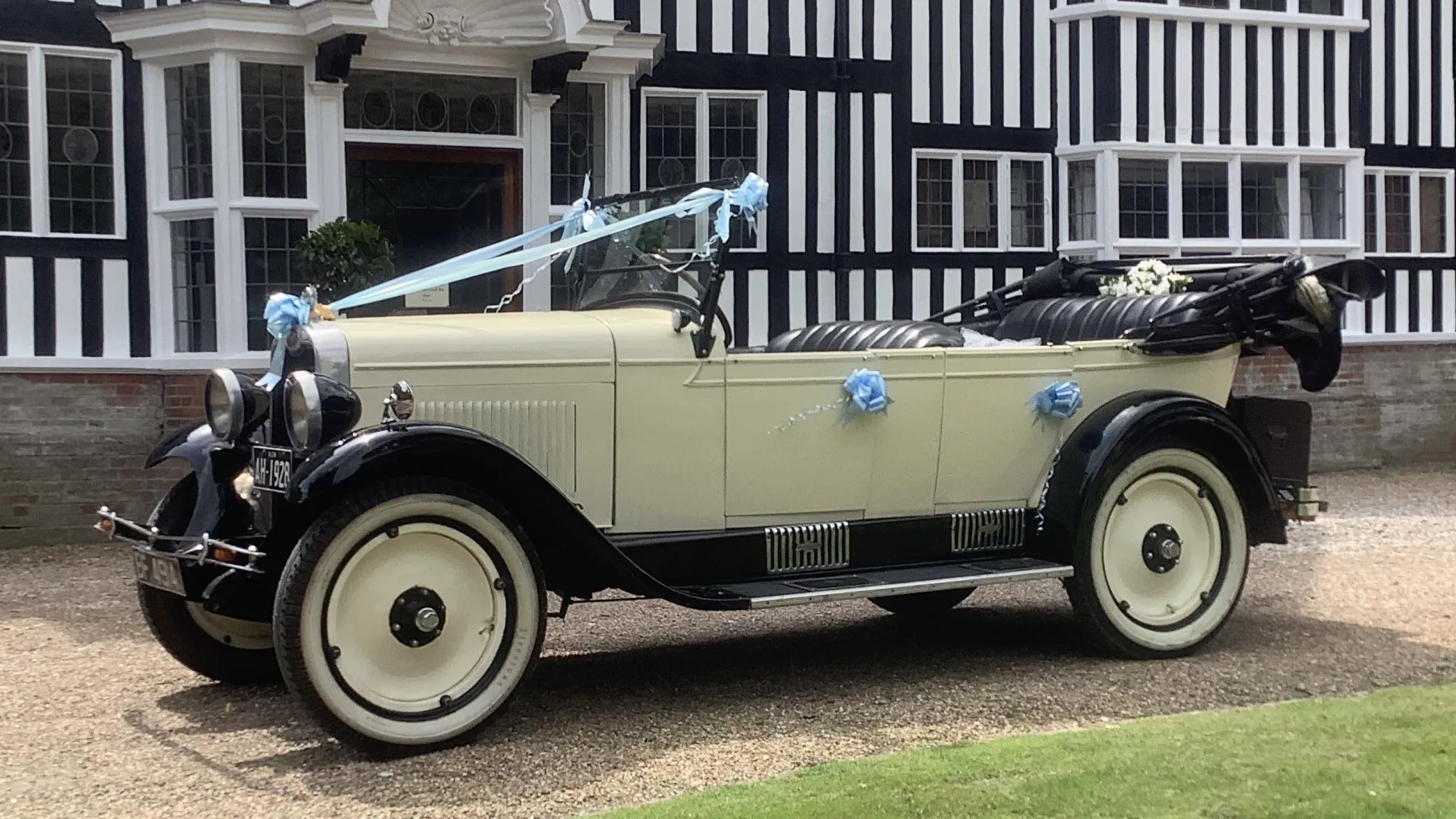 Left sie view of vintage American Chevrolet decorated with light blue ribbons and bows in front of a wedding venue. Convertible roof is open