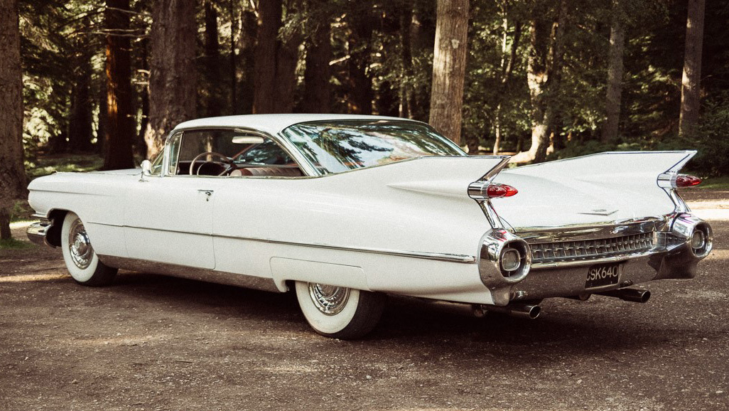 Left rear view of white american Cadillac showing the large chrome bumper and iconic fine tails