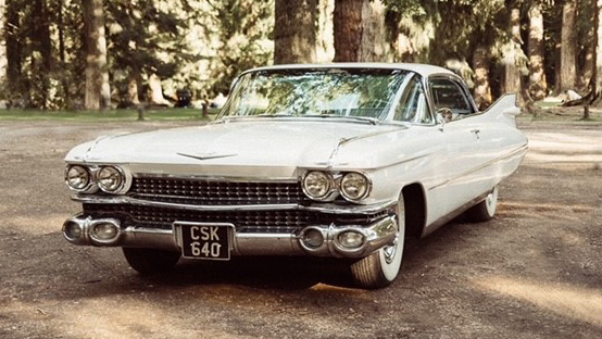 White Cadillac Coupe de Ville parked in a park with trees in the background