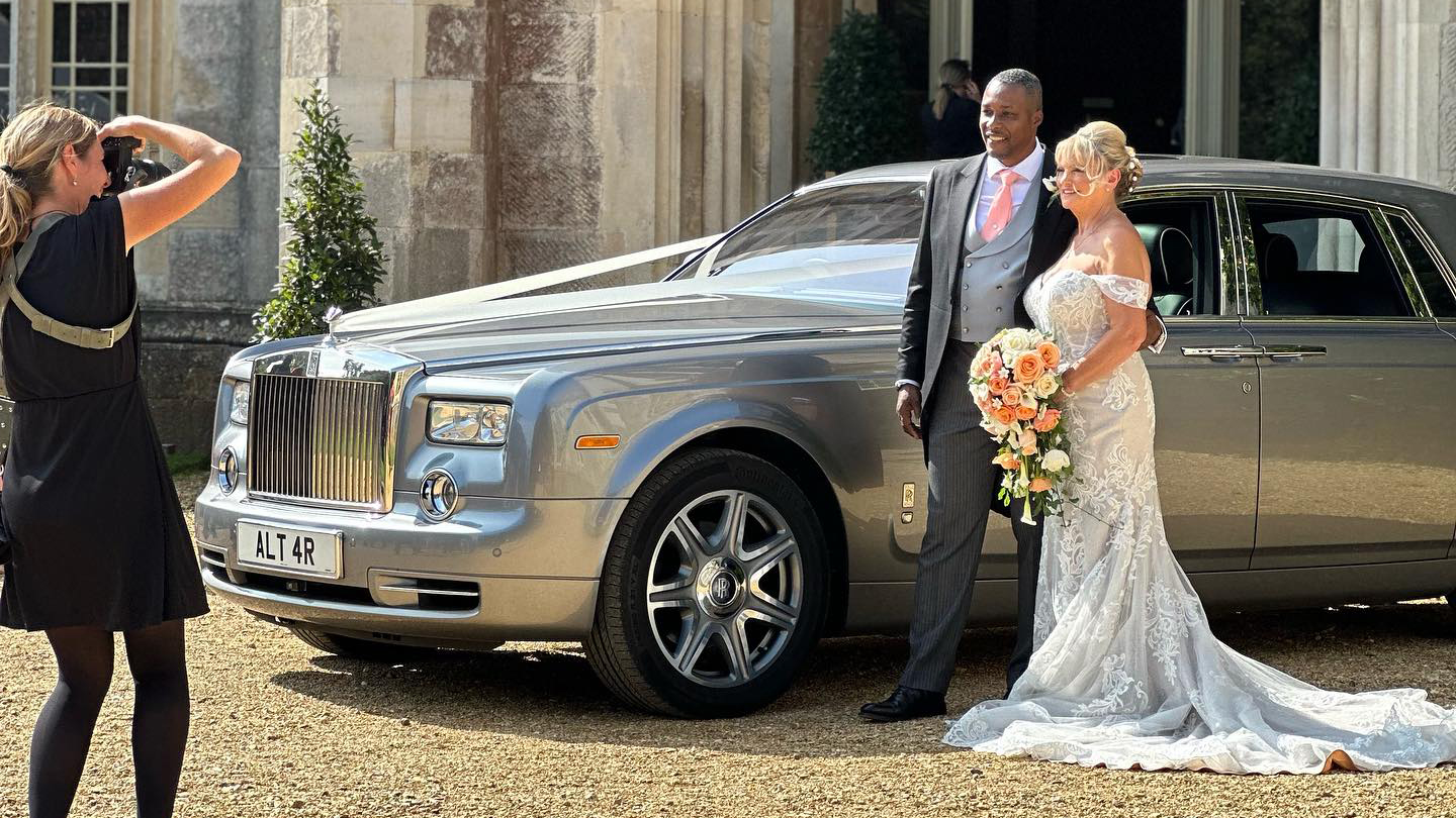 Bride and Groom with Rolls-Royce Phantom decorated with white ribbons and their wedding photographer taking a photo