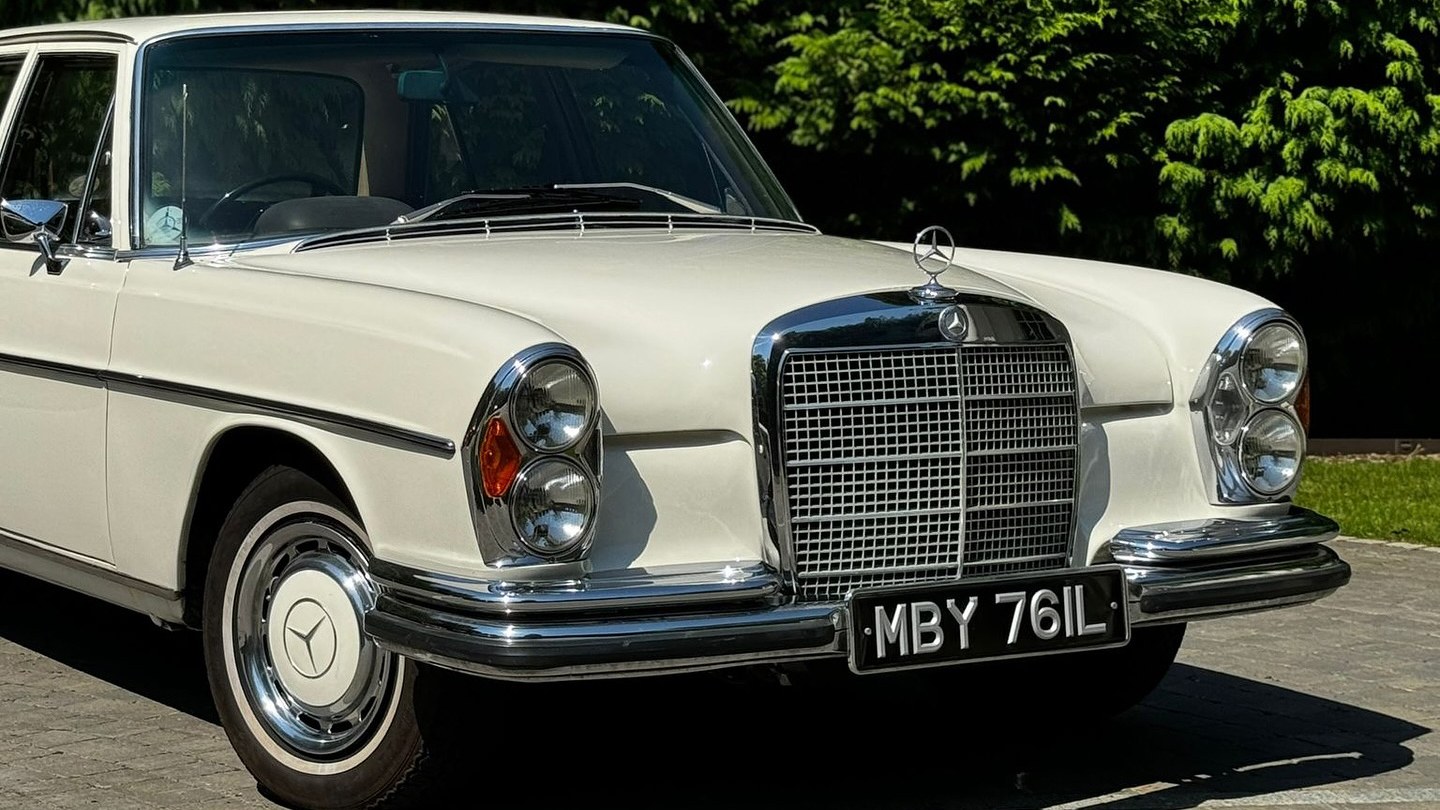 close up photo opf classic mercedes in old english white and its large chrome grill with Mercedes logo on top