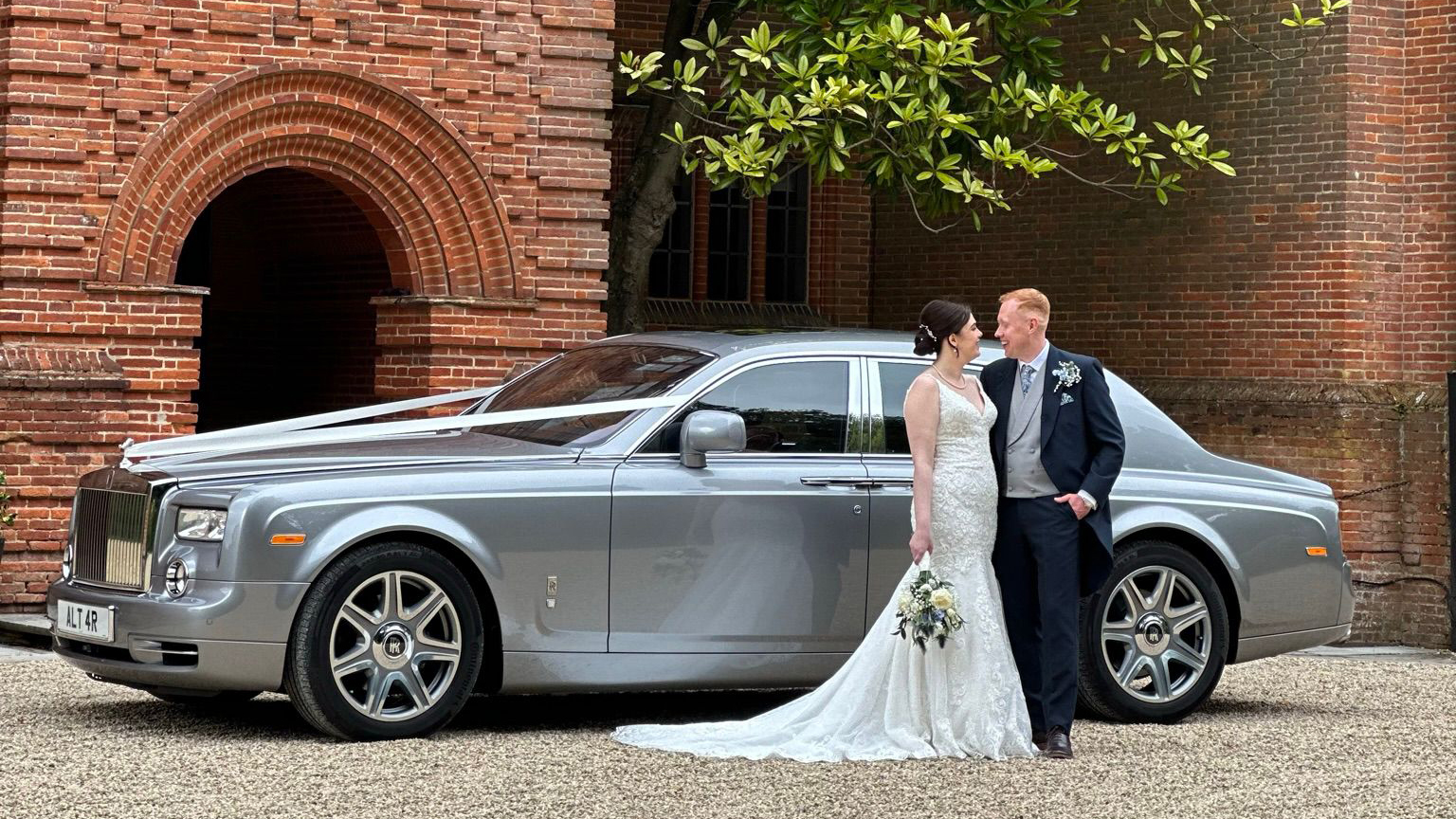 Bride and Groom lookign at each others standing in front of a silver modern Rolls-Royce Phantom