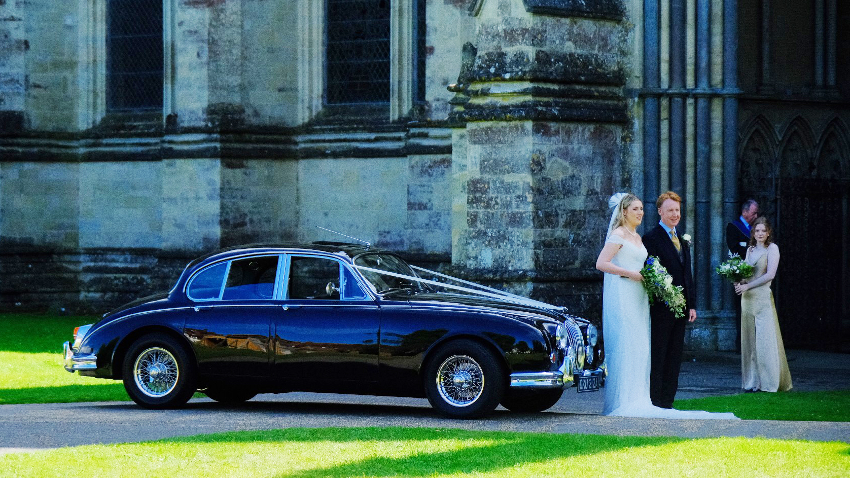 Bride and Groom standing in front of Black Jaguar Mk2 in front of Cathedral.